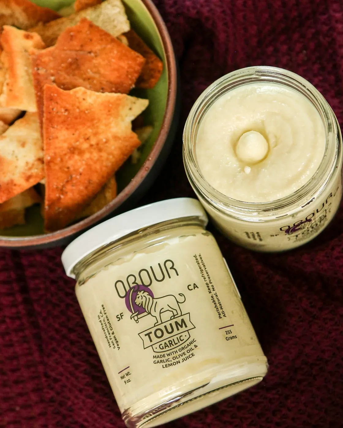A jar of Garlic toum with a bowl of pita chips on a dark red cloth