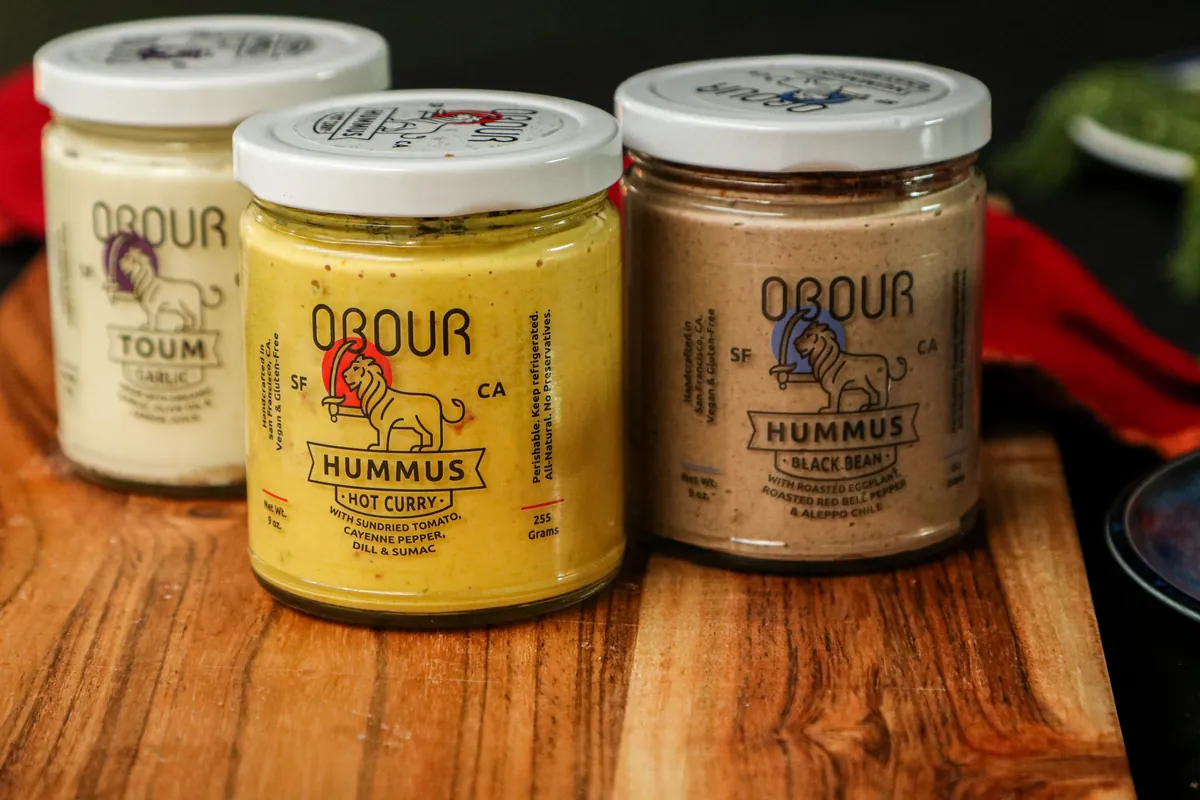 Jars of Obour Garlic toum, Hot Curry hummus and Black Bean hummus on a wooden board