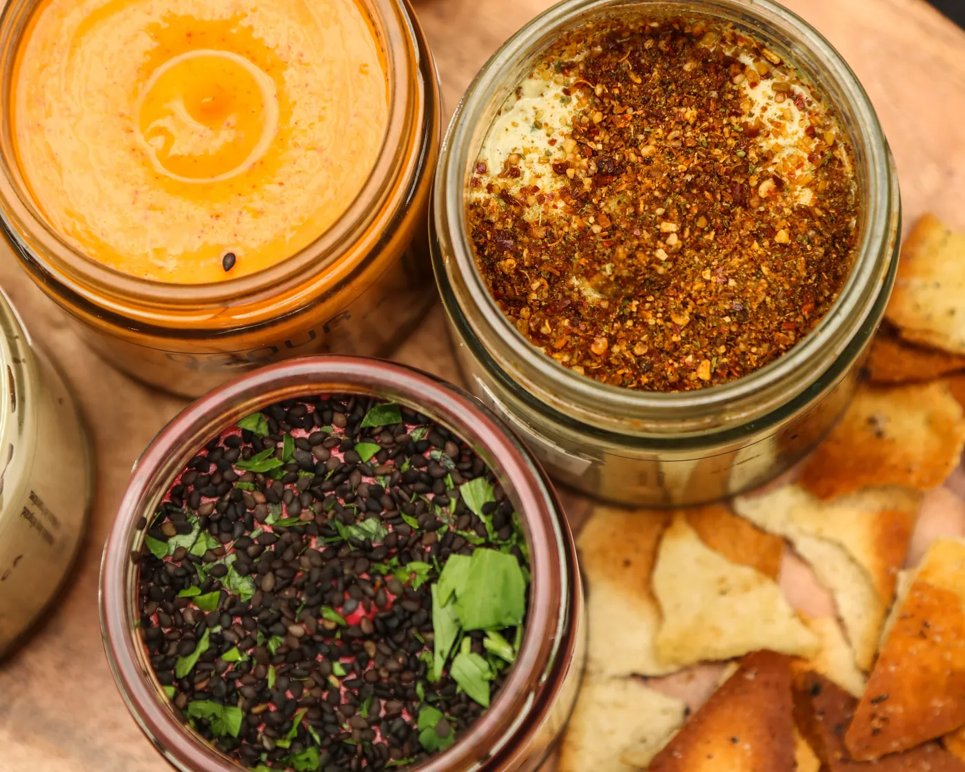 Open jars of Obour hummus topped with spices, with pita chips