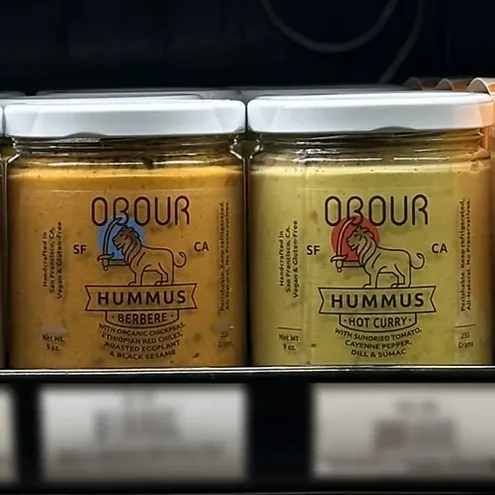 Jars of Obour Berbere and Hot Curry hummus on a grocery store's refrigerated shelf