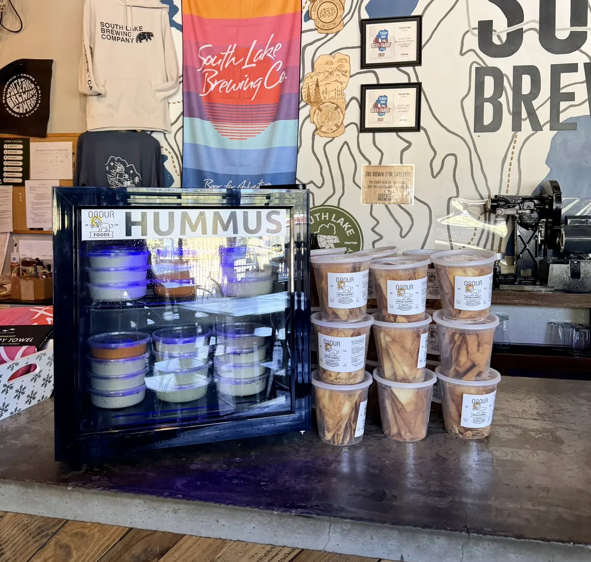 An Obour Hummus Fridge at South Lake Brewing, with tubs of pita chips stacked beside it