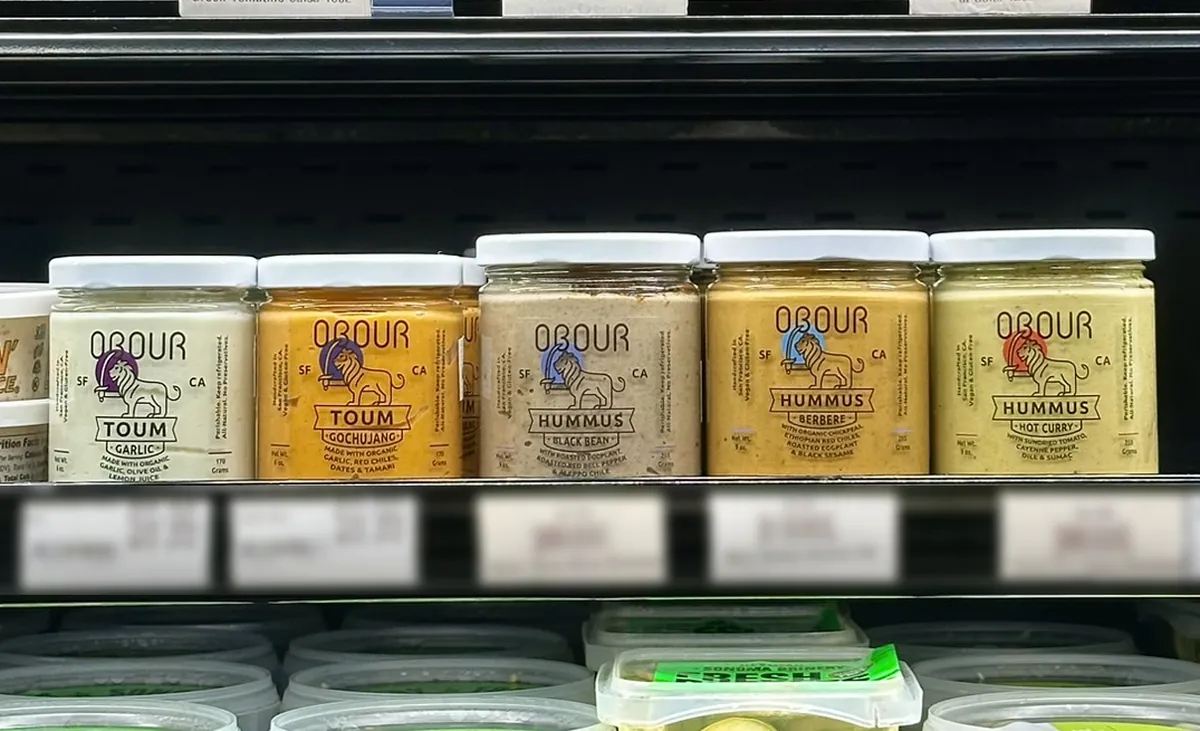 A row of Obour toum and hummus jars in a grocery store deli case